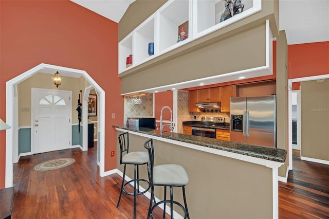 kitchen featuring a towering ceiling, a breakfast bar, dark hardwood / wood-style floors, kitchen peninsula, and stainless steel appliances