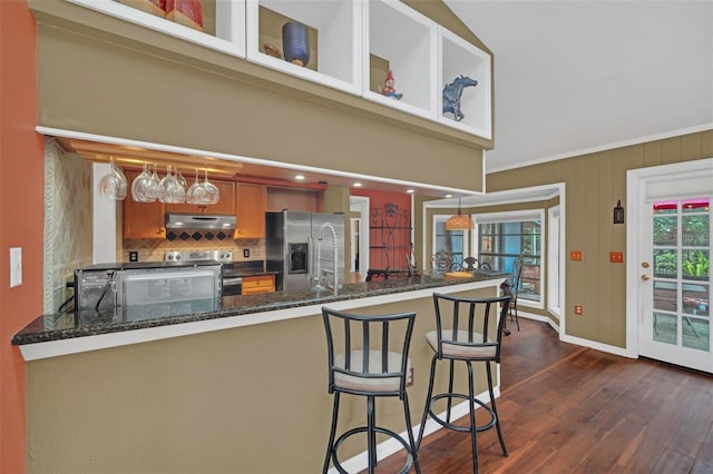 kitchen featuring sink, dark stone countertops, appliances with stainless steel finishes, dark hardwood / wood-style flooring, and kitchen peninsula