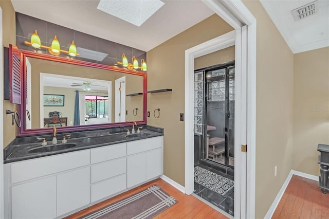 bathroom with wood-type flooring, a skylight, vanity, a shower with door, and ceiling fan