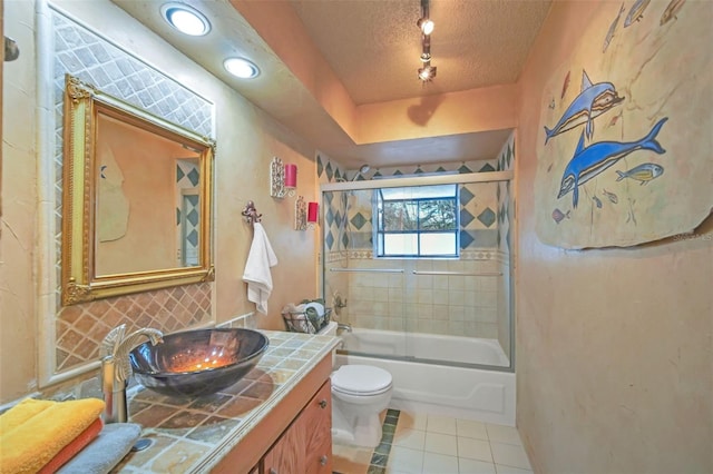 full bathroom with bath / shower combo with glass door, vanity, toilet, tile patterned floors, and a textured ceiling