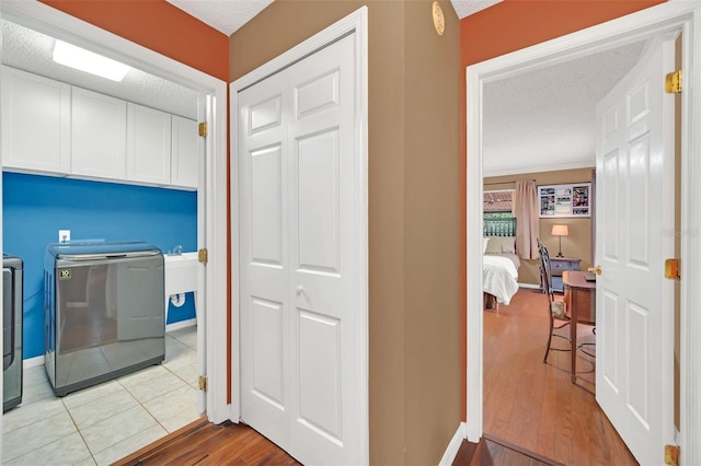 washroom featuring cabinets, light hardwood / wood-style flooring, a textured ceiling, and washing machine and clothes dryer