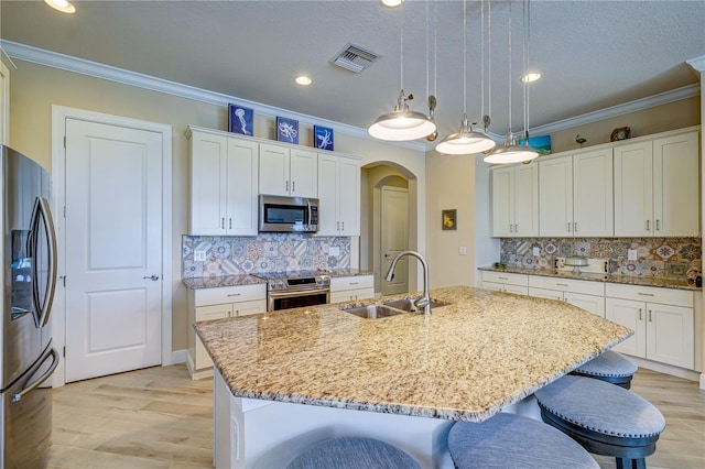 kitchen with sink, ornamental molding, decorative light fixtures, a center island with sink, and appliances with stainless steel finishes