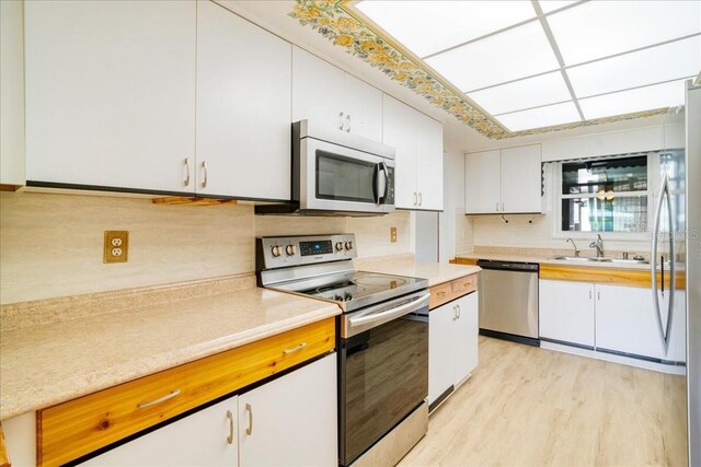 kitchen featuring appliances with stainless steel finishes, light hardwood / wood-style floors, white cabinets, backsplash, and sink