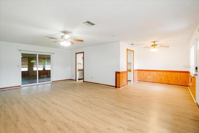 empty room featuring a textured ceiling, wooden walls, ceiling fan, and light hardwood / wood-style flooring