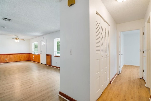 hallway with wooden walls, light hardwood / wood-style floors, and a textured ceiling