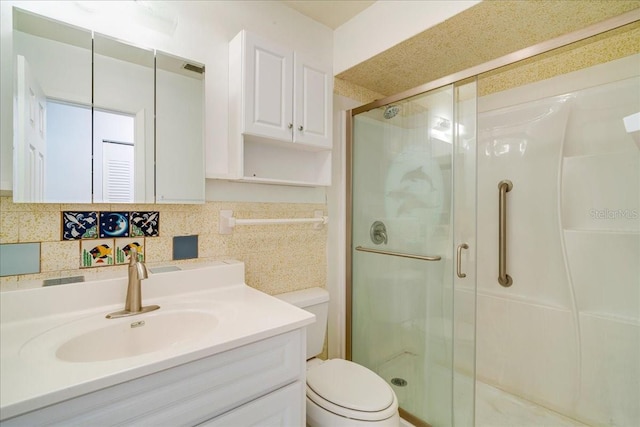 bathroom with vanity, a shower with shower door, toilet, and tasteful backsplash