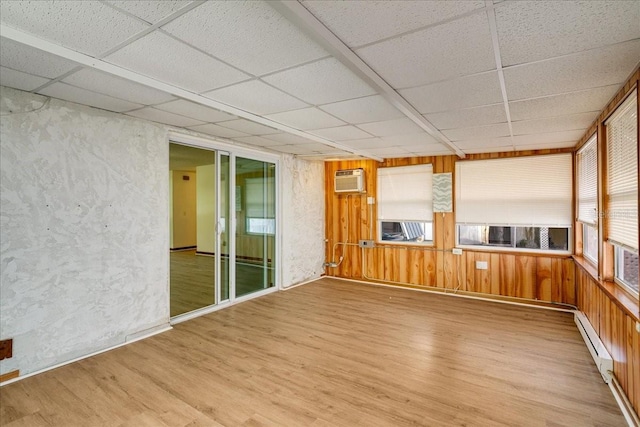 empty room featuring wood walls, a drop ceiling, baseboard heating, hardwood / wood-style floors, and a wall mounted AC