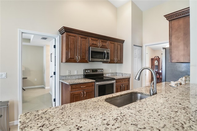 kitchen with light stone counters, appliances with stainless steel finishes, sink, and a high ceiling