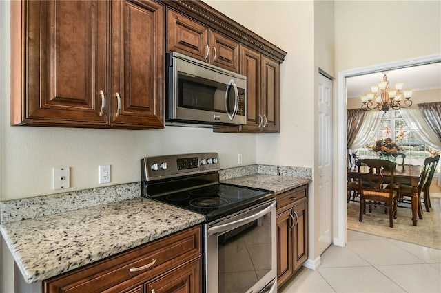 kitchen with an inviting chandelier, light stone countertops, stainless steel appliances, and light tile patterned floors