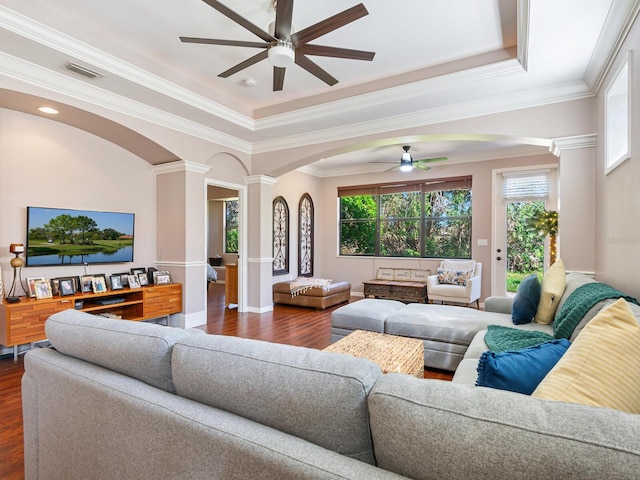 living room with ornate columns, a tray ceiling, ornamental molding, dark hardwood / wood-style flooring, and ceiling fan