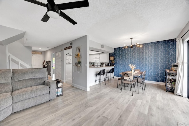 living room with light hardwood / wood-style floors, ceiling fan with notable chandelier, a textured ceiling, and sink