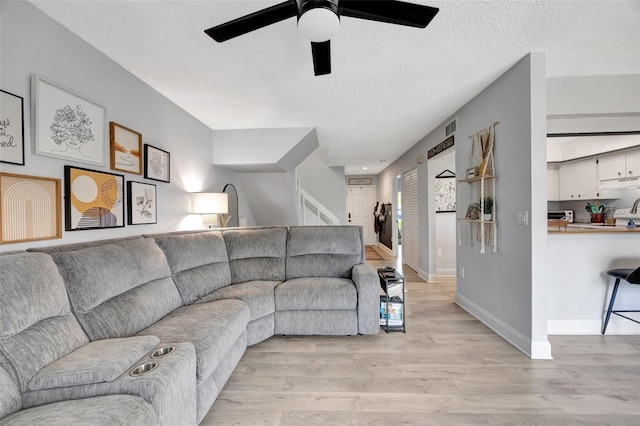 living room featuring light wood-type flooring, a textured ceiling, and ceiling fan