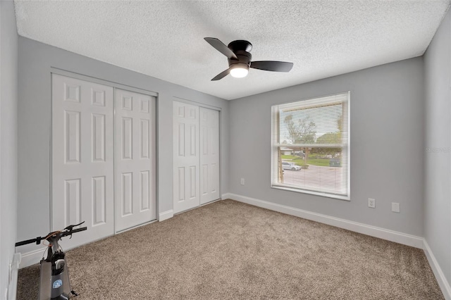 unfurnished bedroom featuring ceiling fan, a textured ceiling, light carpet, and multiple closets