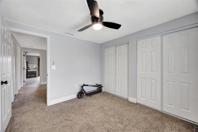 unfurnished bedroom with a textured ceiling, light carpet, ceiling fan, and two closets