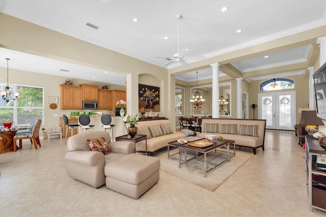 tiled living room featuring french doors, ceiling fan with notable chandelier, ornate columns, and crown molding