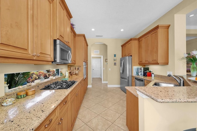 kitchen featuring sink, light tile patterned floors, appliances with stainless steel finishes, light stone counters, and kitchen peninsula