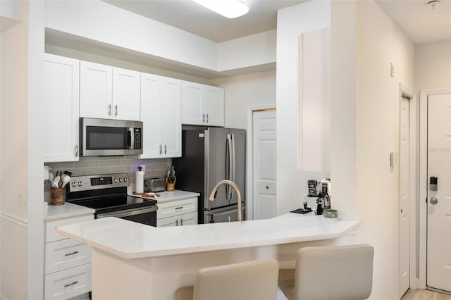 kitchen with white cabinets, appliances with stainless steel finishes, kitchen peninsula, and a kitchen breakfast bar