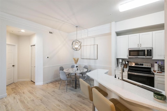 kitchen featuring decorative light fixtures, decorative backsplash, white cabinetry, and appliances with stainless steel finishes