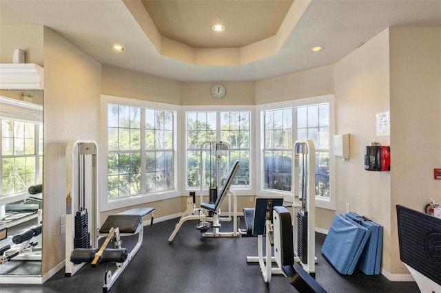 gym featuring a tray ceiling and a healthy amount of sunlight