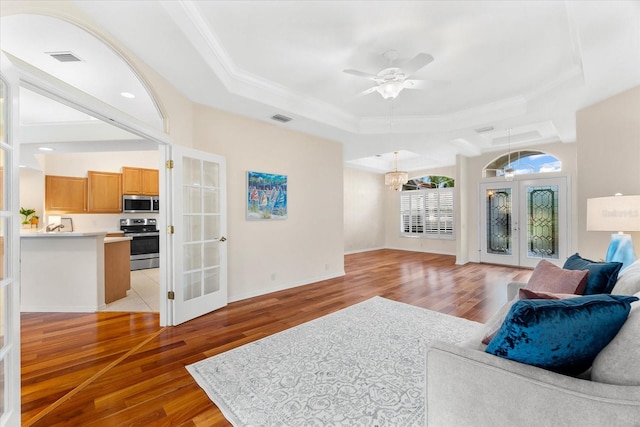 living room featuring ceiling fan with notable chandelier, a raised ceiling, light hardwood / wood-style flooring, and french doors