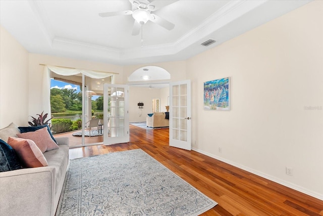 living room featuring hardwood / wood-style floors, french doors, crown molding, ceiling fan, and a tray ceiling