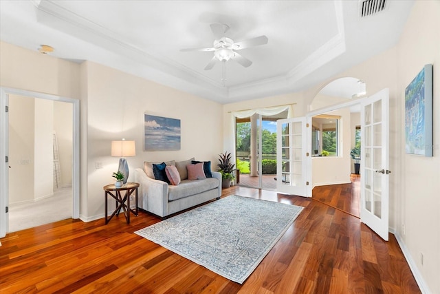 living room with dark wood-type flooring, french doors, crown molding, ceiling fan, and a tray ceiling