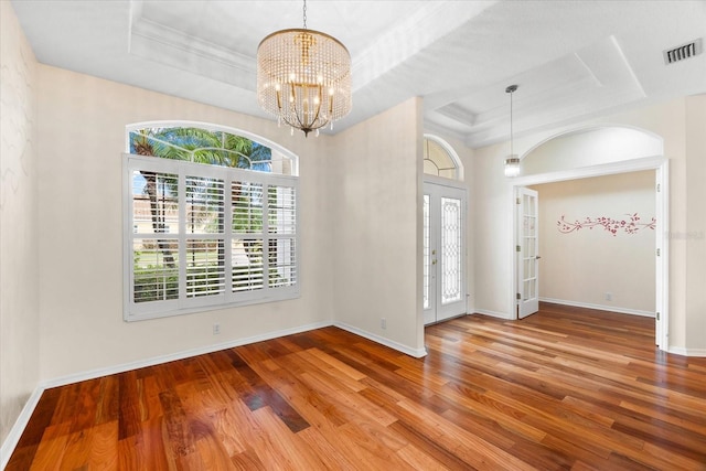 empty room with a raised ceiling, a chandelier, and wood-type flooring