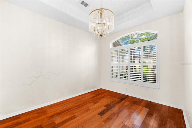 unfurnished room with hardwood / wood-style floors, a raised ceiling, and an inviting chandelier