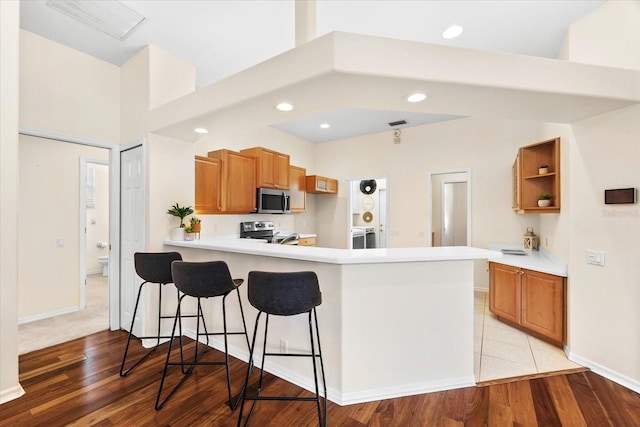 kitchen with kitchen peninsula, a kitchen breakfast bar, stainless steel appliances, and light hardwood / wood-style flooring