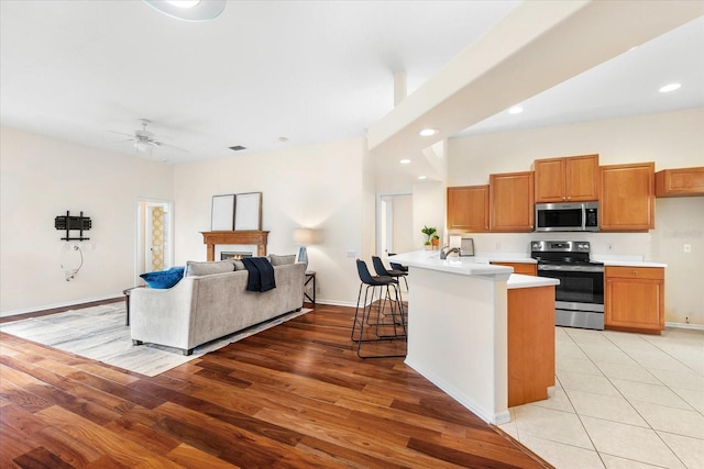 kitchen with ceiling fan, appliances with stainless steel finishes, light hardwood / wood-style floors, a kitchen bar, and kitchen peninsula