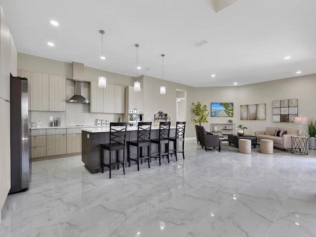 kitchen featuring wall chimney range hood, stainless steel refrigerator, pendant lighting, light brown cabinetry, and a center island