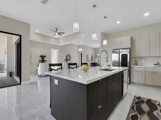 kitchen featuring light stone countertops, light brown cabinets, sink, pendant lighting, and a center island with sink