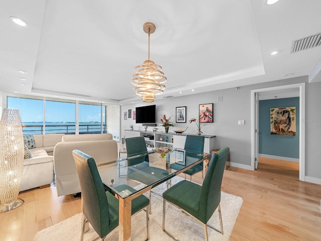 dining area featuring light hardwood / wood-style floors, an inviting chandelier, and a raised ceiling