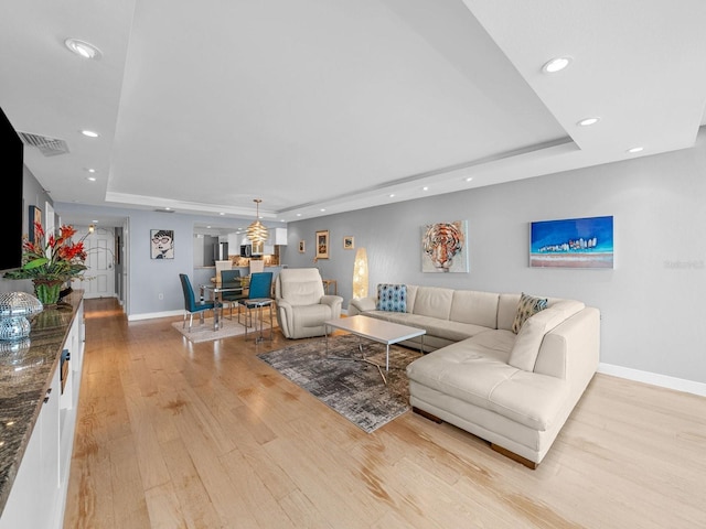 living room with light hardwood / wood-style floors and a tray ceiling