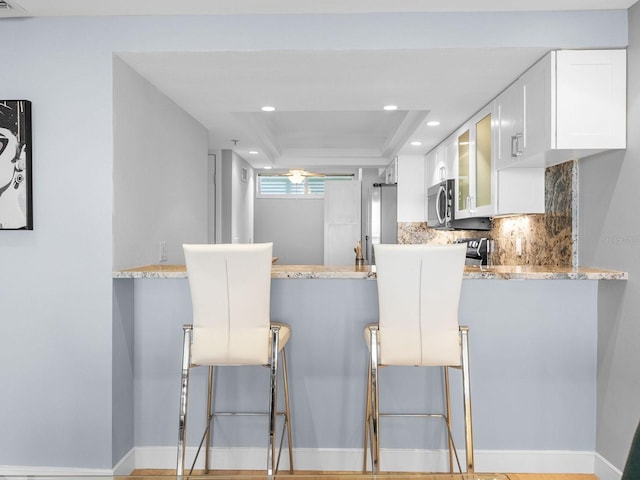 kitchen with light stone counters, white cabinetry, kitchen peninsula, and a tray ceiling