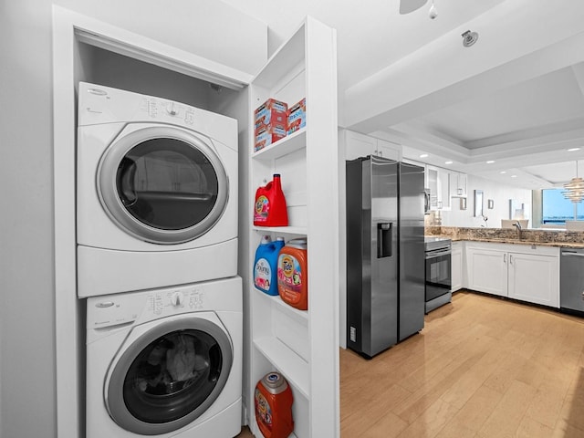 laundry room with stacked washer / drying machine, sink, light wood-type flooring, and a chandelier