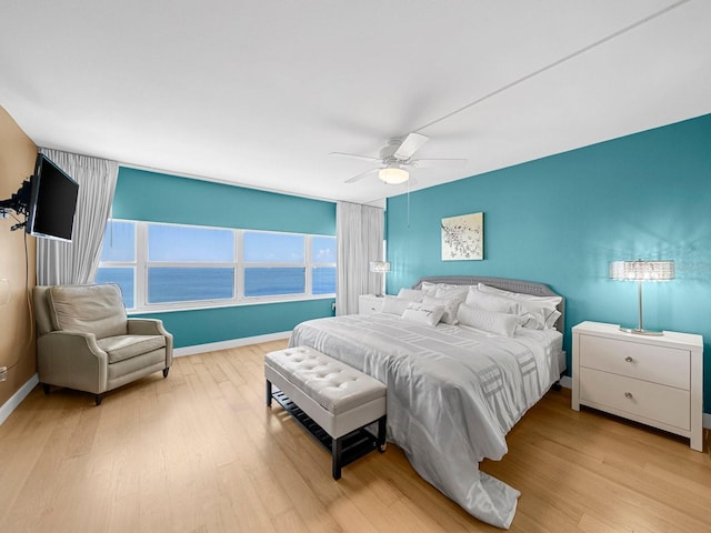 bedroom featuring light hardwood / wood-style flooring, a water view, and ceiling fan