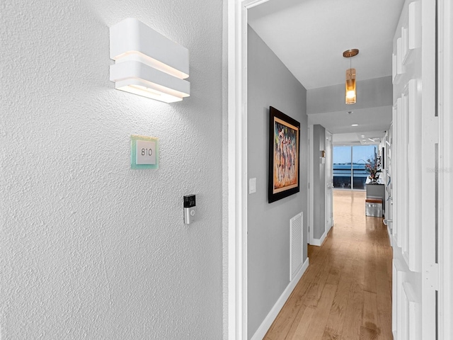 hallway with light wood finished floors, visible vents, and baseboards