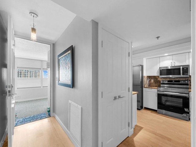 hall with light wood-type flooring, visible vents, and baseboards