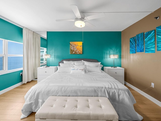 bedroom featuring baseboards, a ceiling fan, light wood-style flooring, an accent wall, and a water view