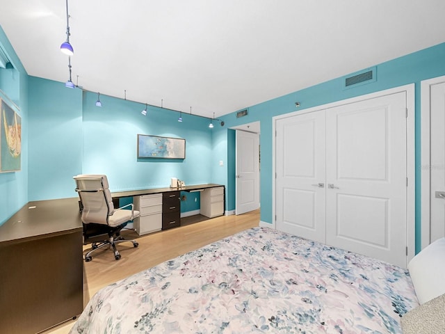 bedroom featuring baseboards, visible vents, built in study area, wood finished floors, and a closet