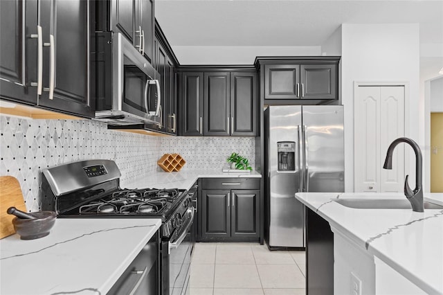 kitchen featuring backsplash, appliances with stainless steel finishes, light tile patterned floors, light stone countertops, and sink