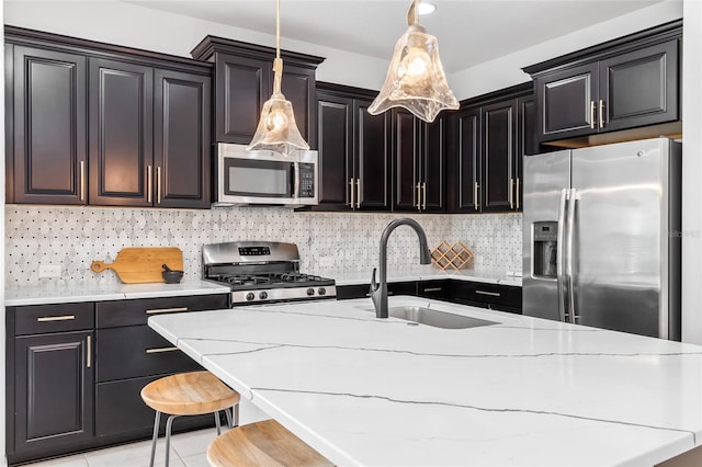 kitchen with light tile patterned floors, sink, hanging light fixtures, stainless steel appliances, and a breakfast bar