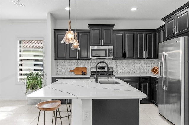 kitchen featuring light stone counters, appliances with stainless steel finishes, backsplash, and a center island with sink