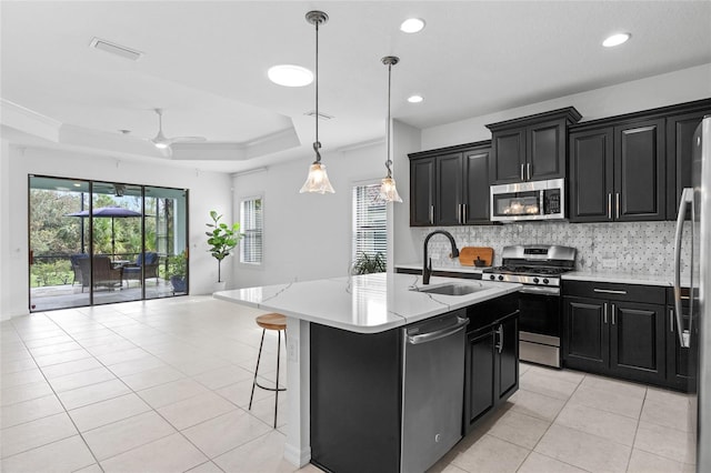 kitchen featuring sink, backsplash, stainless steel appliances, decorative light fixtures, and a kitchen island with sink