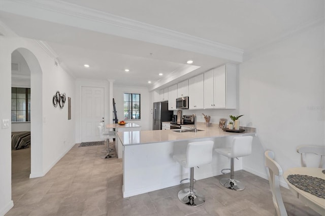 kitchen featuring a kitchen bar, kitchen peninsula, white cabinetry, stainless steel appliances, and ornamental molding