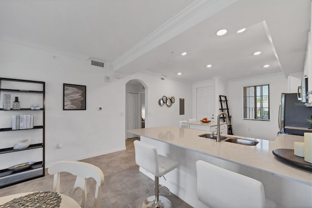 kitchen with a kitchen breakfast bar, ornamental molding, sink, light stone counters, and stainless steel refrigerator