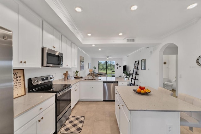 kitchen with kitchen peninsula, a kitchen breakfast bar, stainless steel appliances, white cabinets, and crown molding