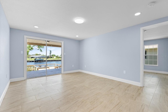 spare room featuring recessed lighting, a water view, and baseboards