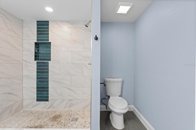 bathroom featuring a tile shower, toilet, and wood-type flooring